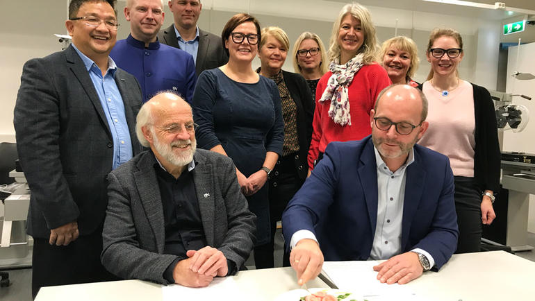 Rektor Petter Aasen spanderte kake på Martin Rostrup i anledning signeringen. USN-ansatte i bakgrunnen. Foto