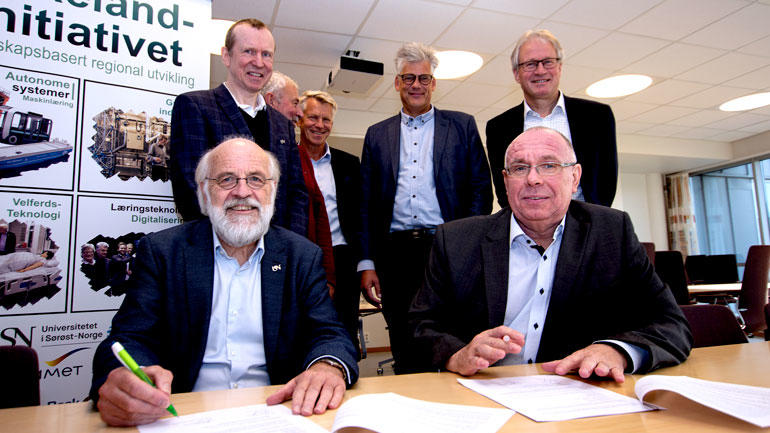 Rektor Petter Aasen og Yaras Ole-Jacob SIljan signerer avtalen og smiler til kamera. De andre står bak som vitner.