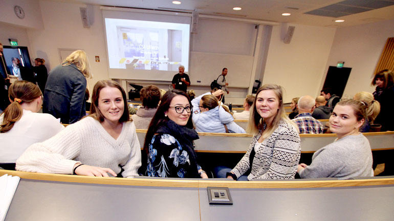 Fire kvinnelige studenter snur seg mot kamera i et auditorium