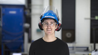 En mannlig ingeniørstudent med hørselvern smiler og ser rett i kamera