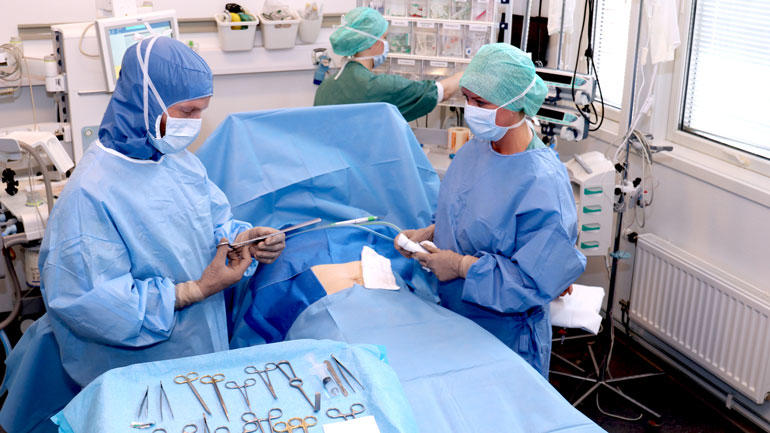 Operasjonssykepleiestudenter i aksjon med full påkledning operasjonsklær  i operasjonssal med pasient på senga.  