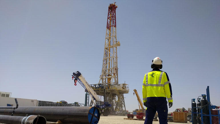Illustrasjonsbilde av et boretårn i Dubai med Kelda Drilling Controls og der en ingeniør i gul refleksjakke som står med ryggen til og ser på 
