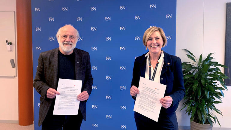 Rektor Petter Aasen og fylkesrådmann Lisbeth Eek Svensson står oppstilt med avtalen i hånda og smiler til kamera foran blå USN-vegg. 