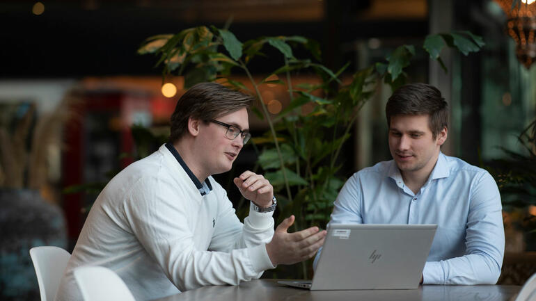 Håkon sittende sammen med sjefen Kristoffer Karud, ser i en laptopå. Blurry bakgrunn i kontorlandskap.