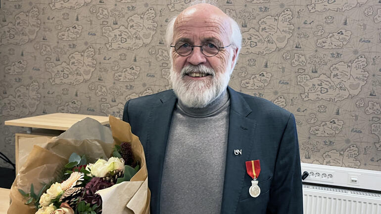 Portrett av Petter Aasen i halvprofil med medaljen på dressjakka og holder en blomsterbukett.
